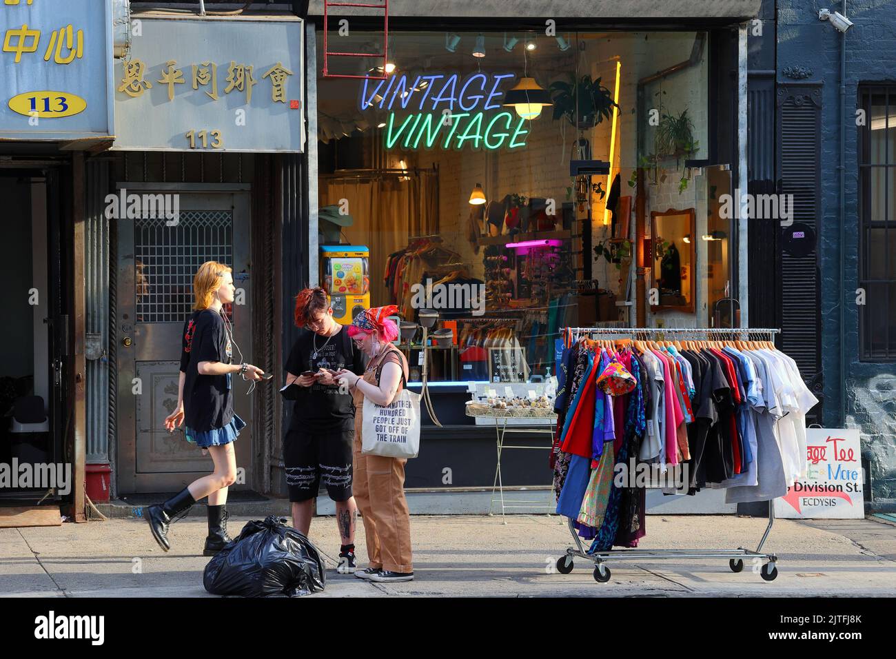 Gen Z visitors to Manhattan 'Dimes Square' Chinatown/Lower East Side  outside a vintage clothing store on their phone searching for travel directions. Stock Photo