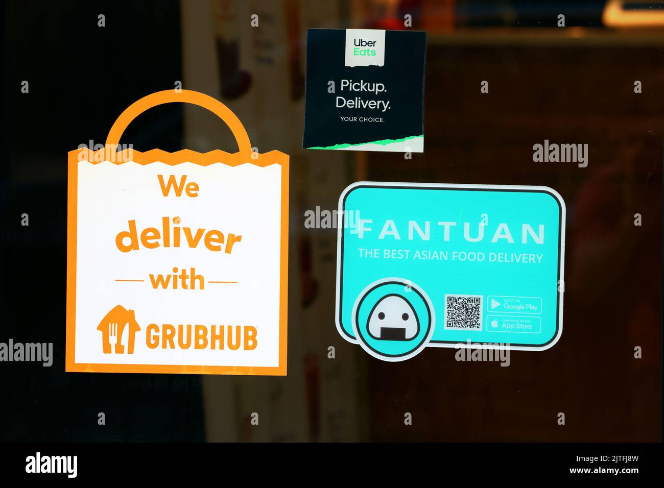 Fantuan, Grubhub, Uber Eats food delivery services app stickers on a door to a restaurant. Stock Photo