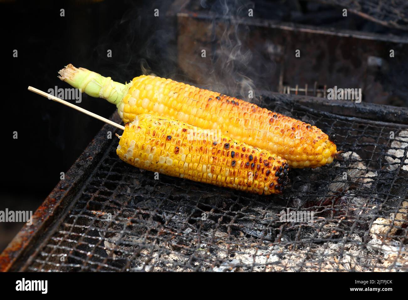 Grilled corn on the cob sizzling on a charcoal grill at a street fair. bbq corn barbeque corn on the grill. Stock Photo