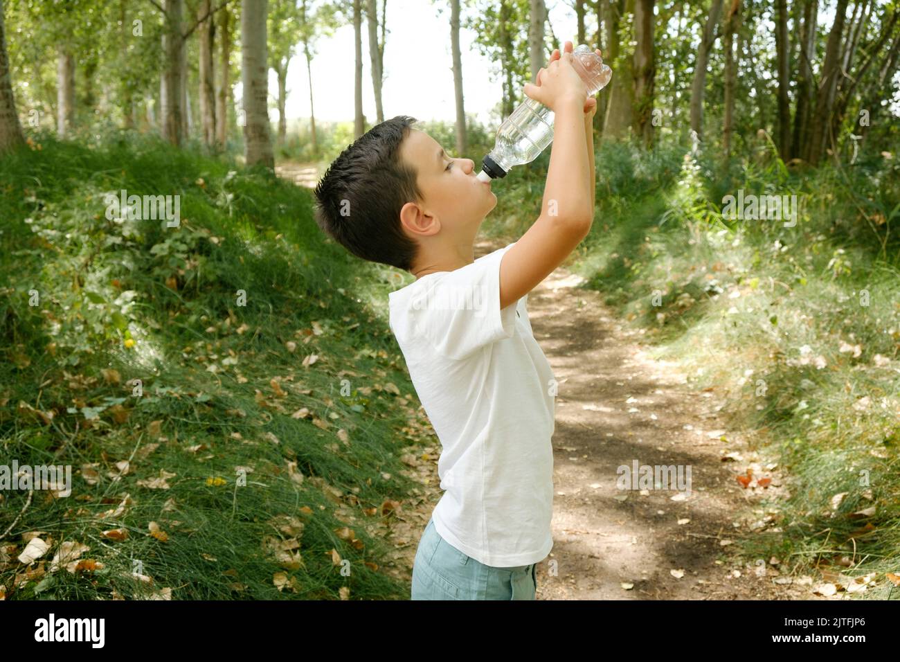 child drinks bottled water during a nature hike. Hydrating in hot summer Stock Photo