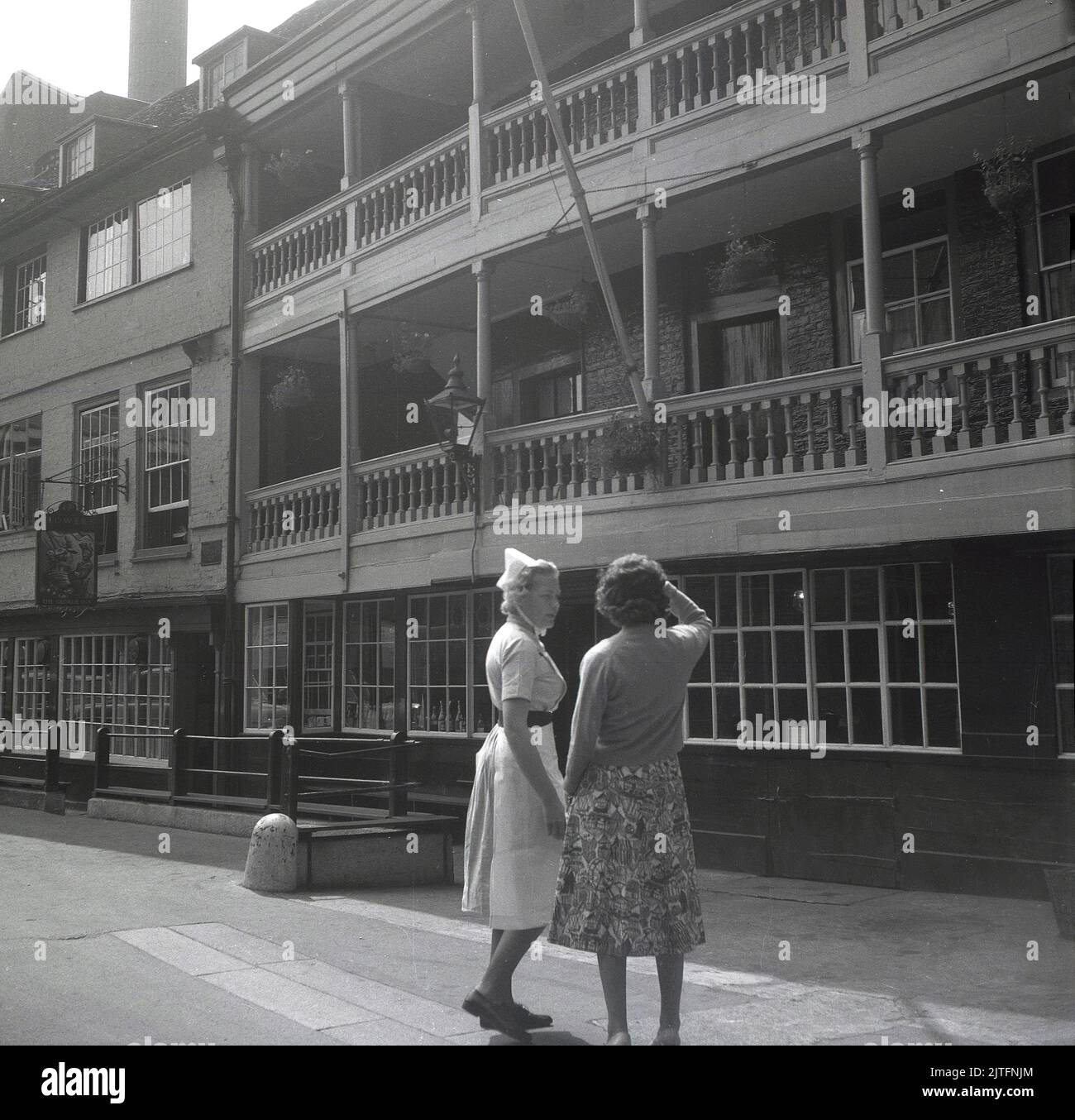 1963, historical, a lady and a nurse standing outside the historic tavern, the George Inn, located off Borough High Street in Southwark, London, England, UK. Guy's Hospital, a large NHS hospital is nearby. The famous public house, The George Inn is the only surviving galliered coaching inn in London. Stock Photo