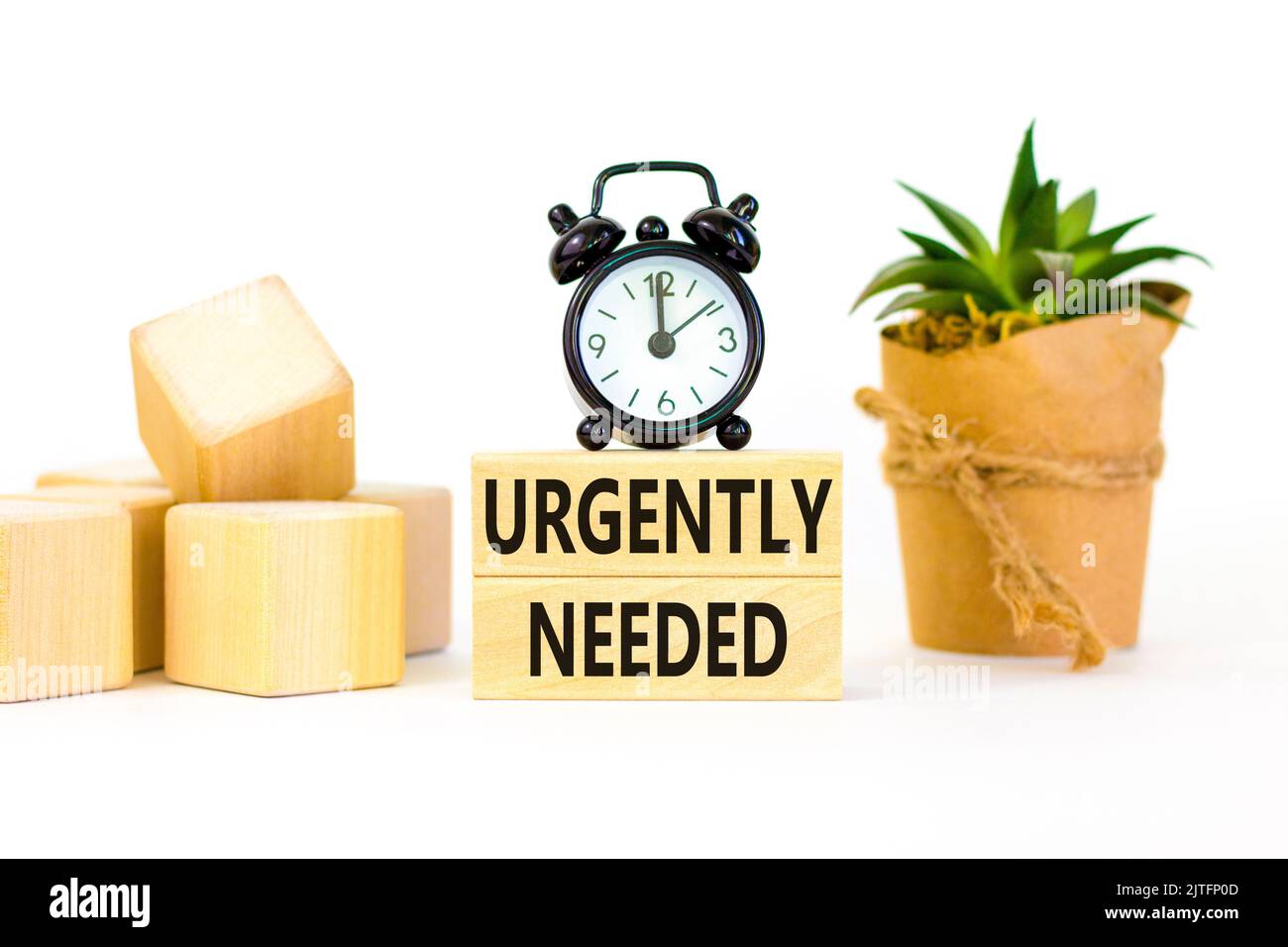Urgently needed symbol. Concept words Urgently needed on wooden blocks on a beautiful white table white background. Black alarm clock. Business and ur Stock Photo
