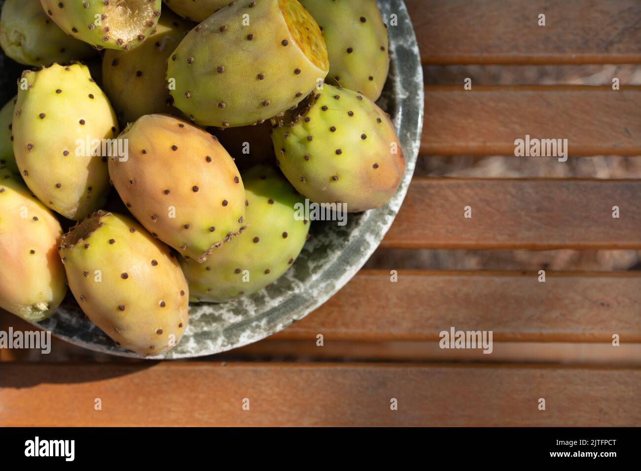 Several ripe prickly pear fruits lie in a ceramic bowl. The bowl stands on a base made of rustic wood. There is space for text. Stock Photo