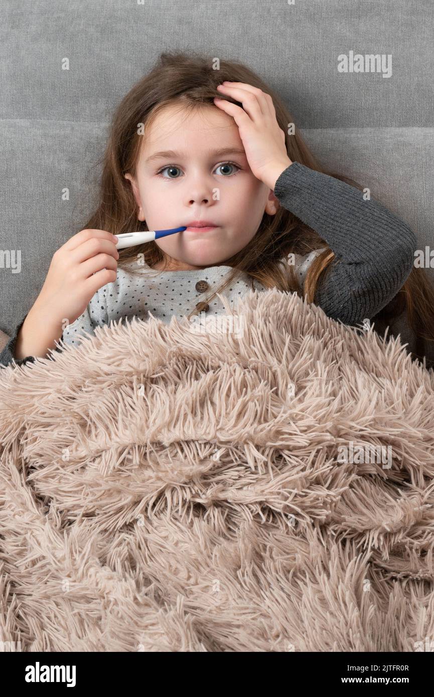 A cute little girl is lying in bed sick, the child measures the