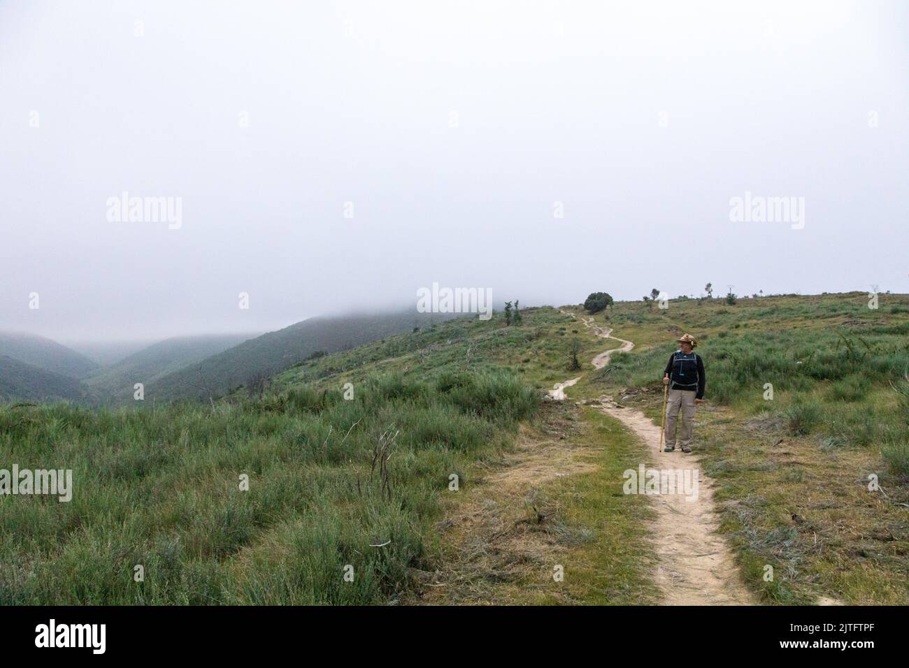 Foggy Camino Morning at El Acebo de San Miguel, Castilla y Leon, Spain, a single male pilgrim walking down the hill Stock Photo