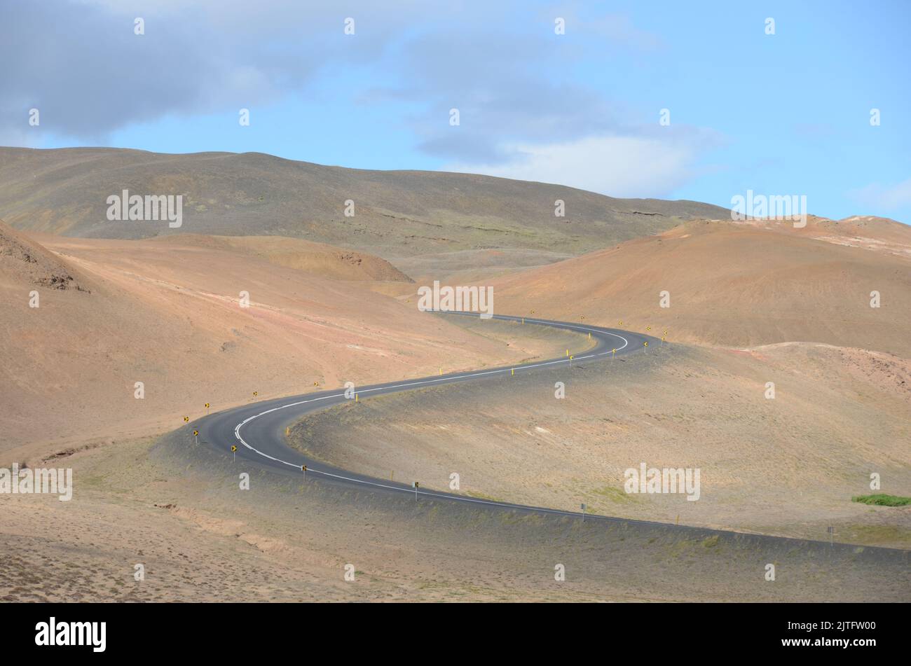 An aerial view of winding asphalt road through desert under blue cloudy ...