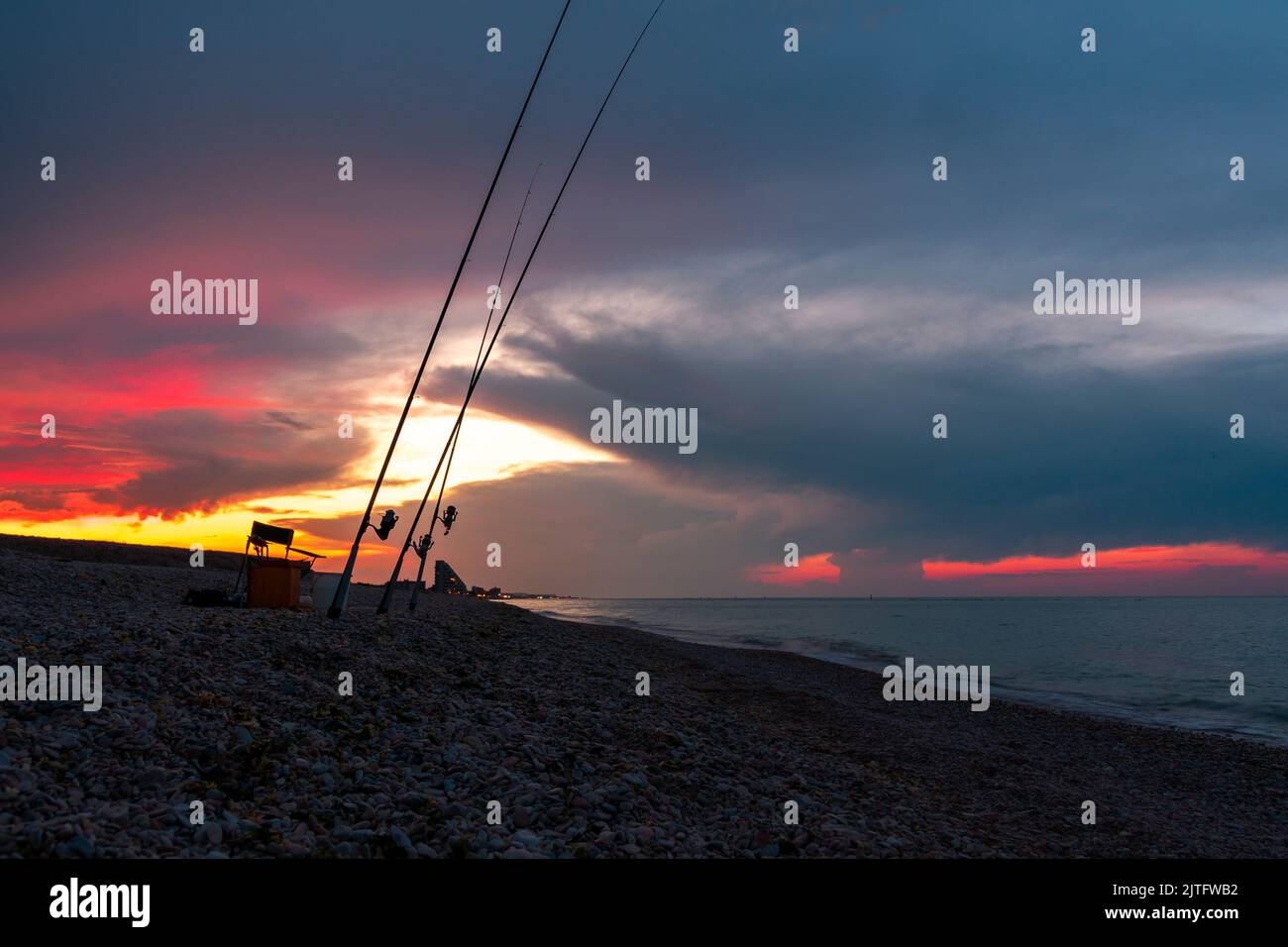 Fishing rods on the shore of the sea against the background of a dramatic sunset. Beautiful sunset over the sea. Night fishing. Stock Photo