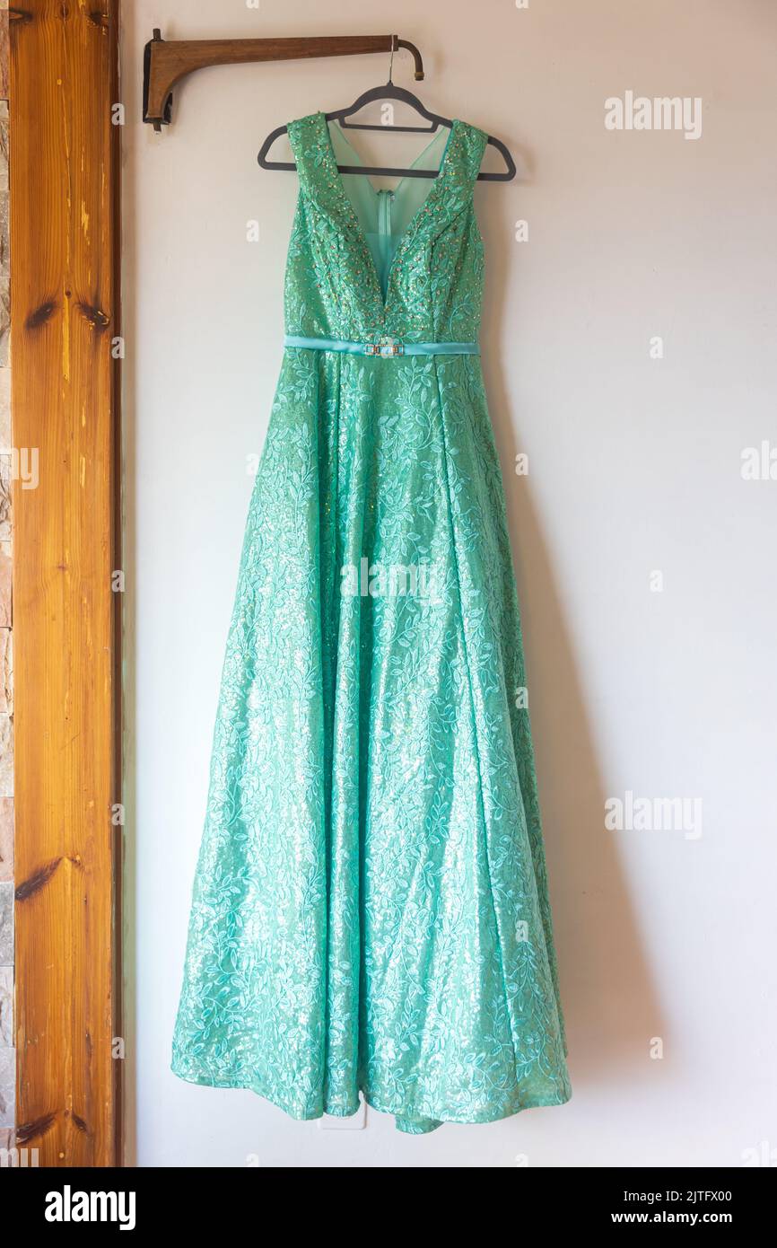 A long green bridesmaid dress with embroidery and sequins is on a hanger on the wall Stock Photo