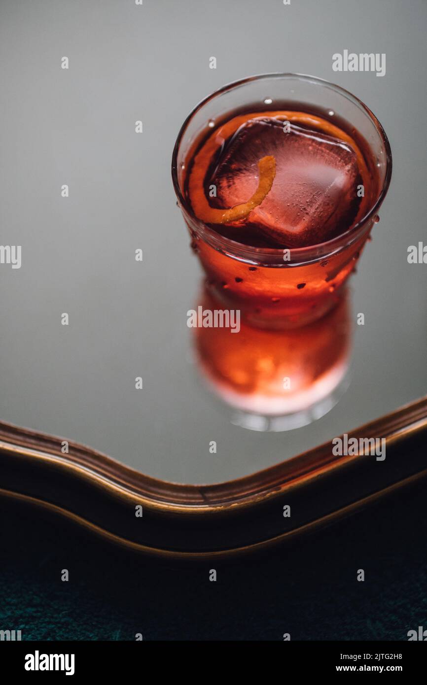 red negroni cocktail with piece of orange and large ice cube in glass
