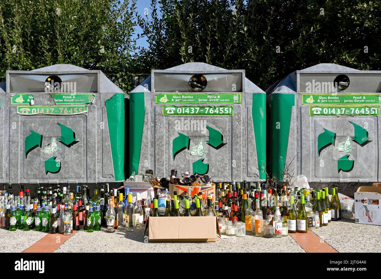 Newport, Pembrokeshire, Wales - August 2022: Large number of wine bottles left alongside recycling bins which are full Stock Photo