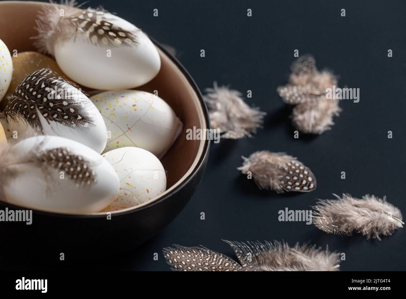 easter eggs with feathers in bowl on black table Stock Photo