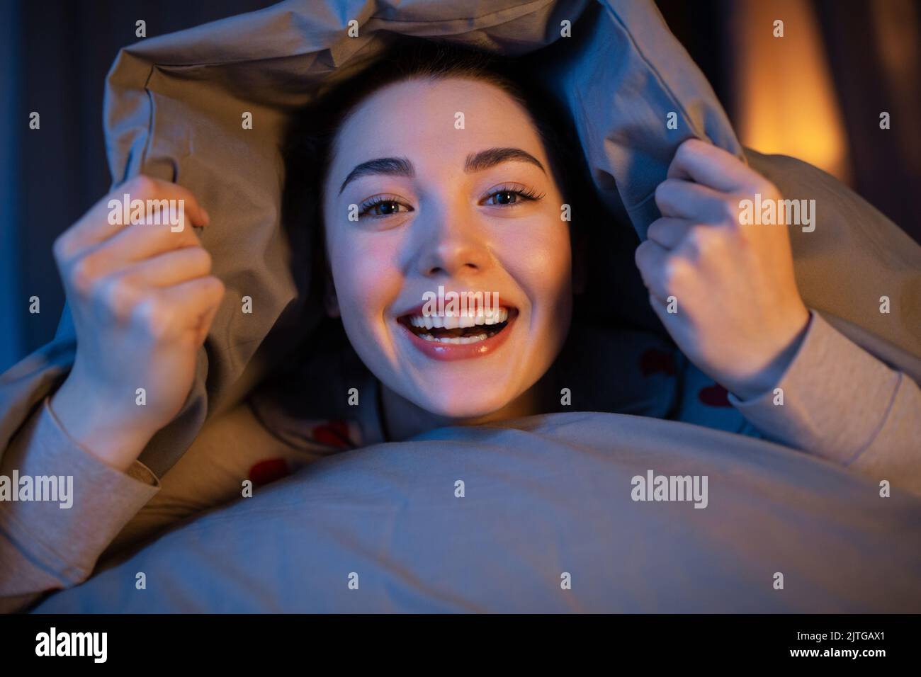 happy teenage girl lying under blanket in bed Stock Photo Alamy