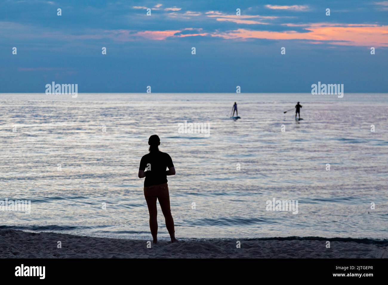 Union Pier, Michigan - A woman watches as two young people propel their stand up paddleboards to the shore of Lake Michigan at the end of a day. Stock Photo