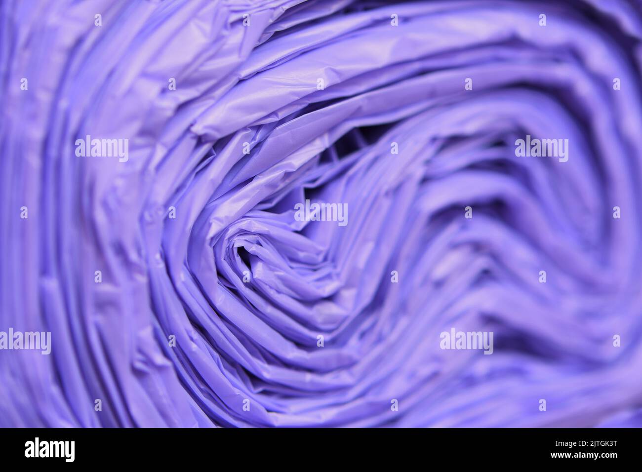 An extreme close-up of the end of a tightly packed roll of non-recyclable purple rubbish/garbage/trash bags Stock Photo