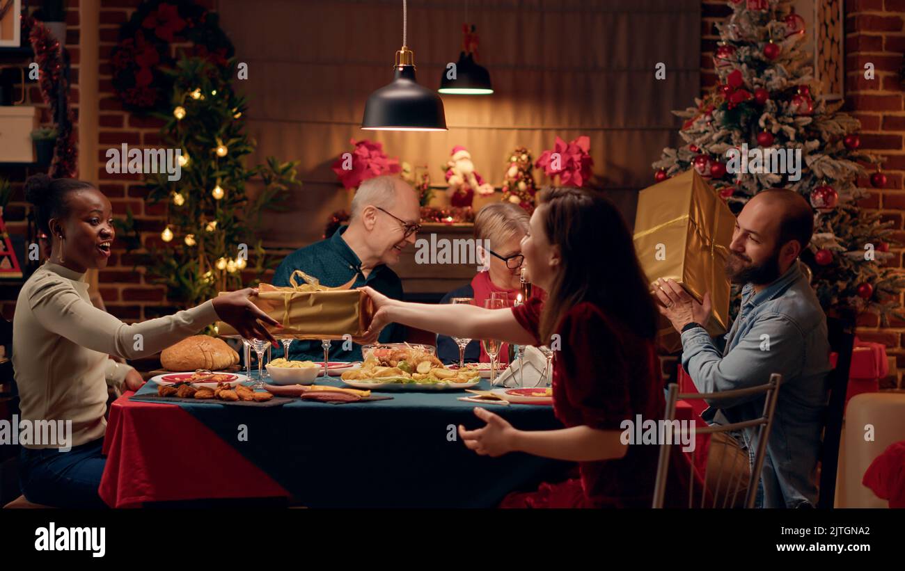 Festive family members sitting at Christmas dinner table while giving ...