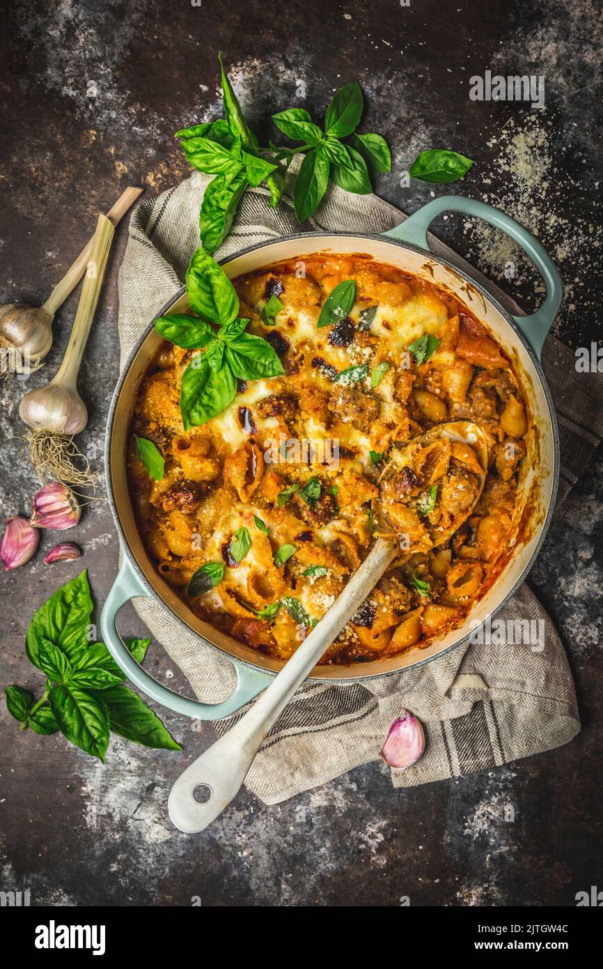 Baked pasta with cheese sauce and sausages in Dutch oven, basil garnish