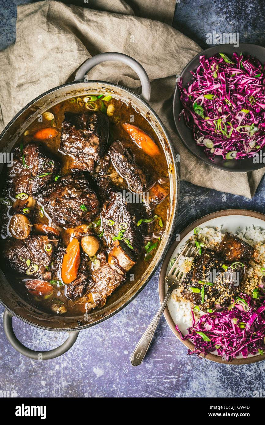 Beef short ribs in Dutch oven with shredded red cabbage on side and plated serving Stock Photo