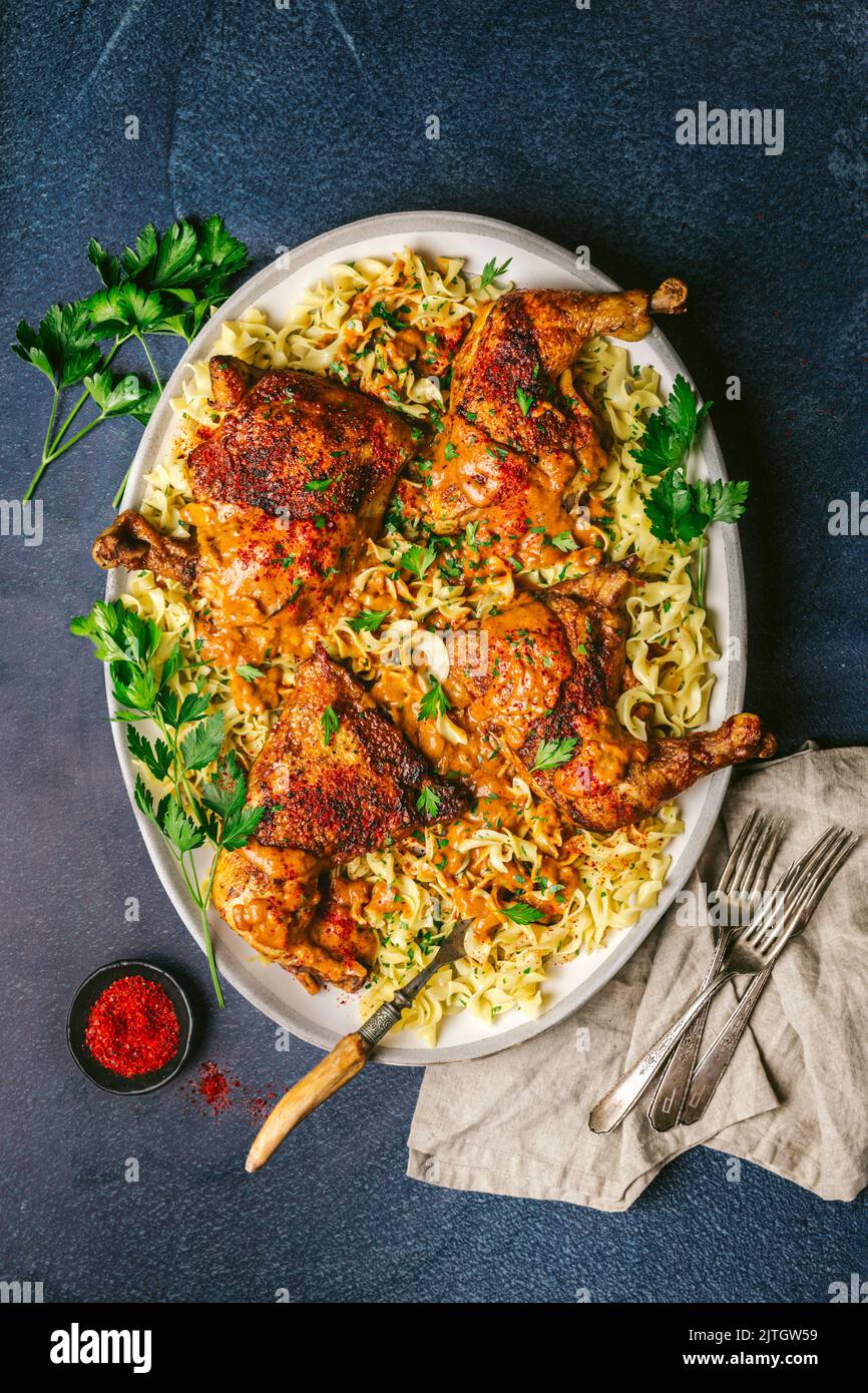 Chicken paprikash thighs over noodles with parsley on serving platter