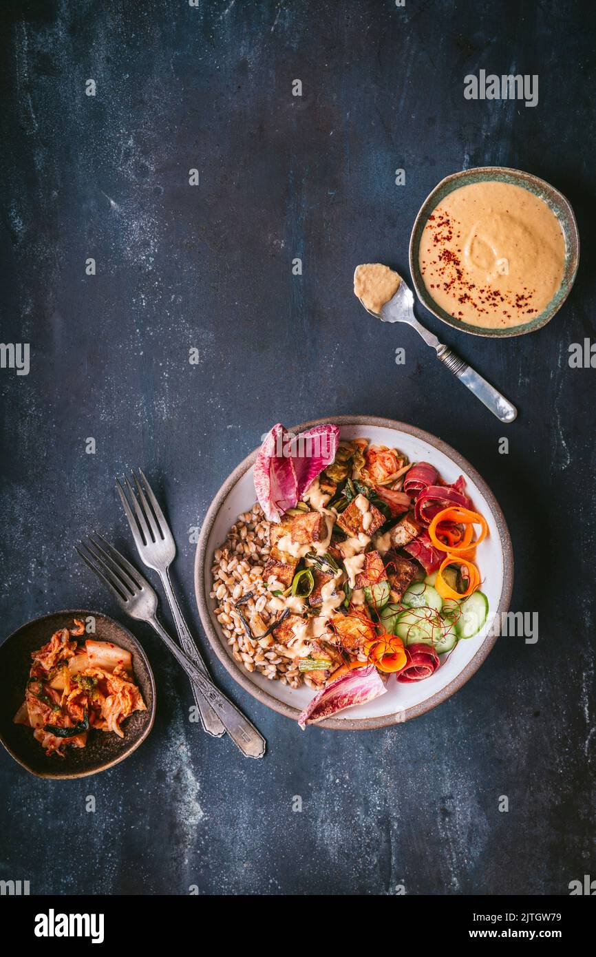 Farro and tofu grain bowl serving with raw vegetables, kimchi and sauce