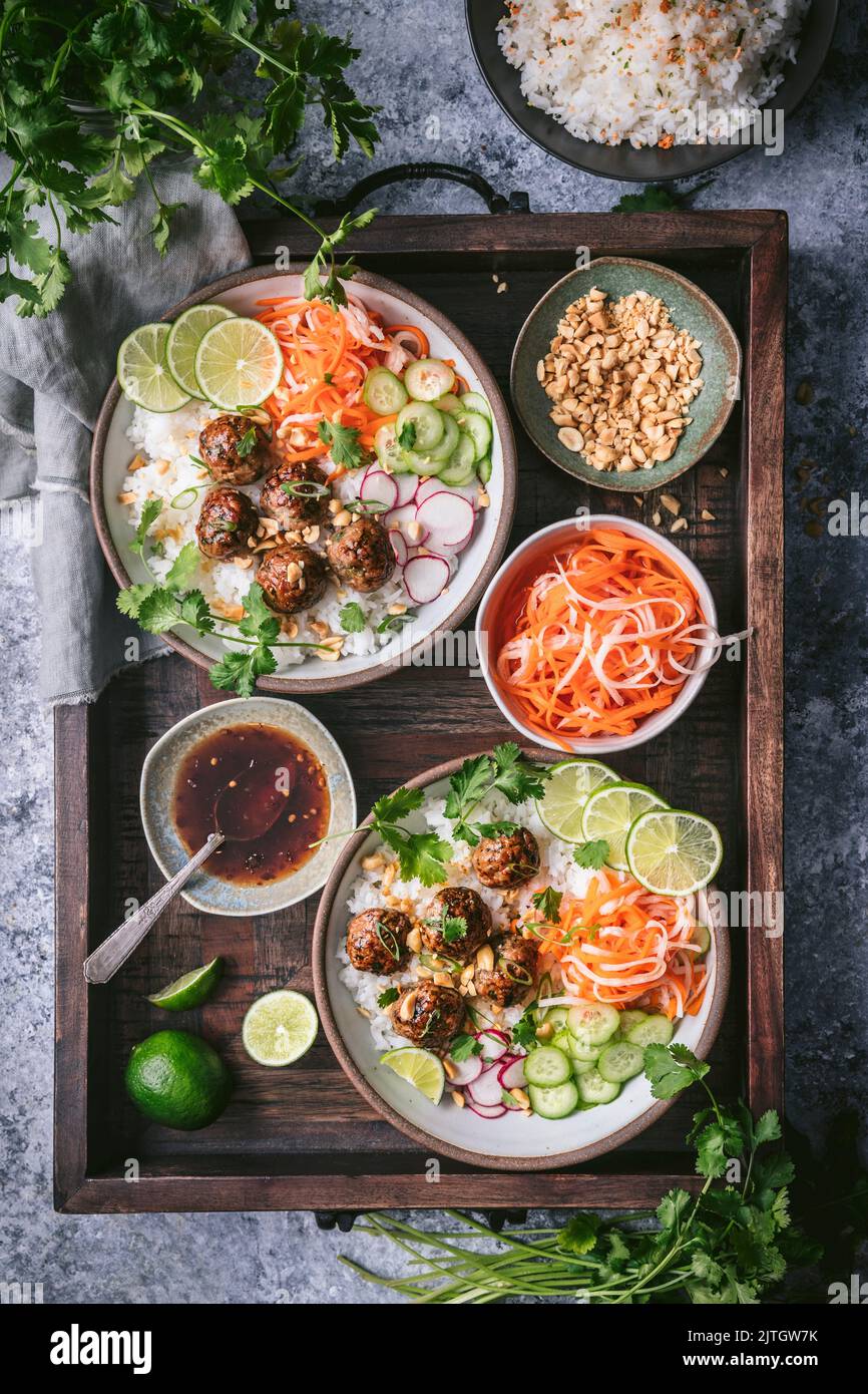 Meatball Rice Bowls on wood tray with colorful pickled vegetables, rice, limes, herbs and peanuts Stock Photo