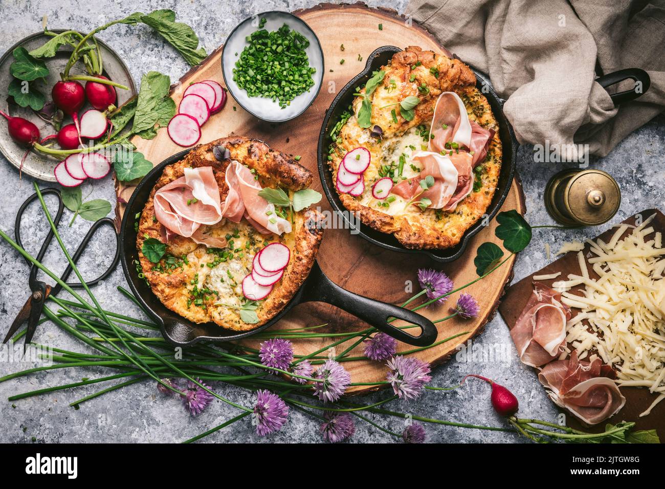 Flat lay of Mini Dutch Babies in Cast Iron Skillets with Cheese, Prosciutto and Radishes Stock Photo
