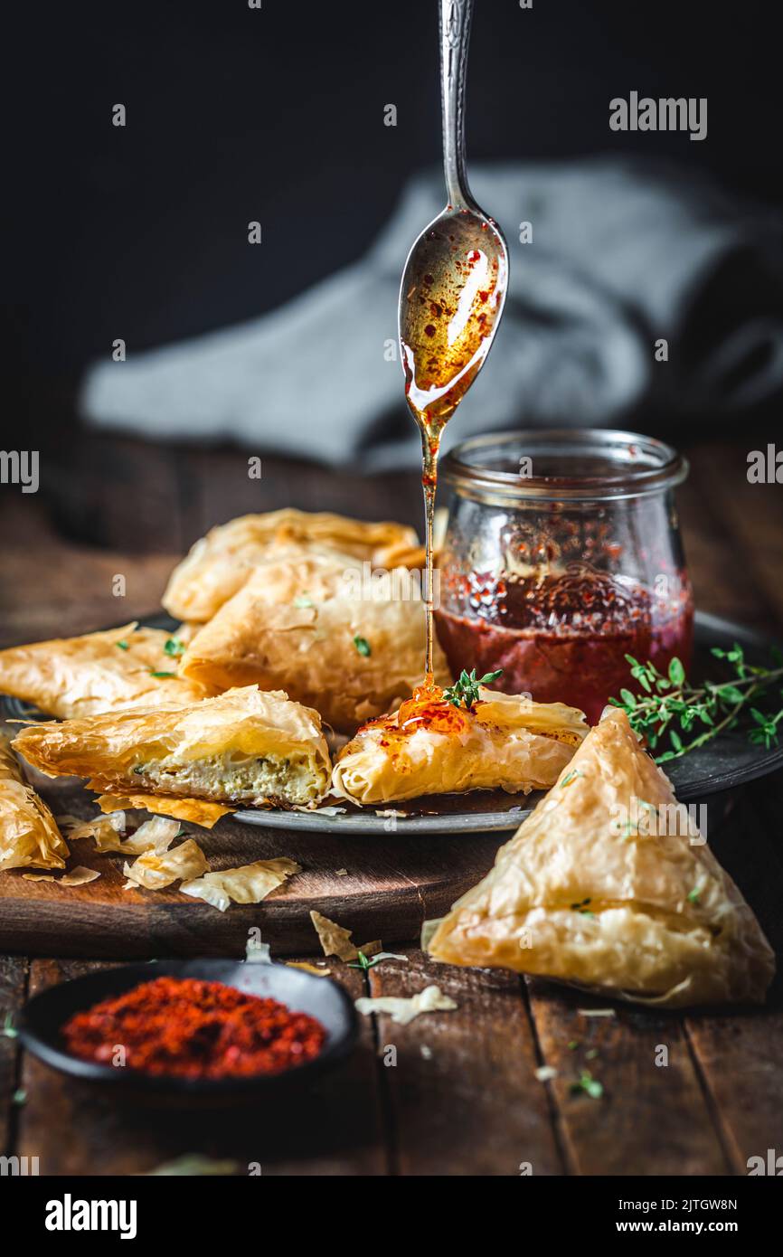 Spicy honey being drizzled over Phyllo Goat Cheese Triangles with chili