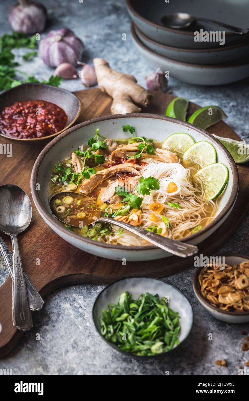 Bowl of Chicken Ginger Rice Noodle Soup on wood board with garnishes