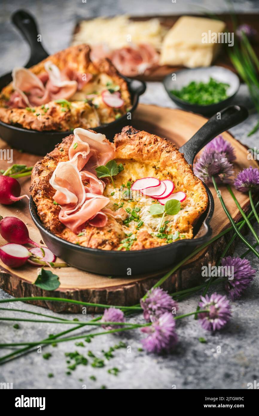 Front shot of Mini Dutch Babies in Cast Iron Skillets with Prosciutto, Chive flowers and Radishes Stock Photo