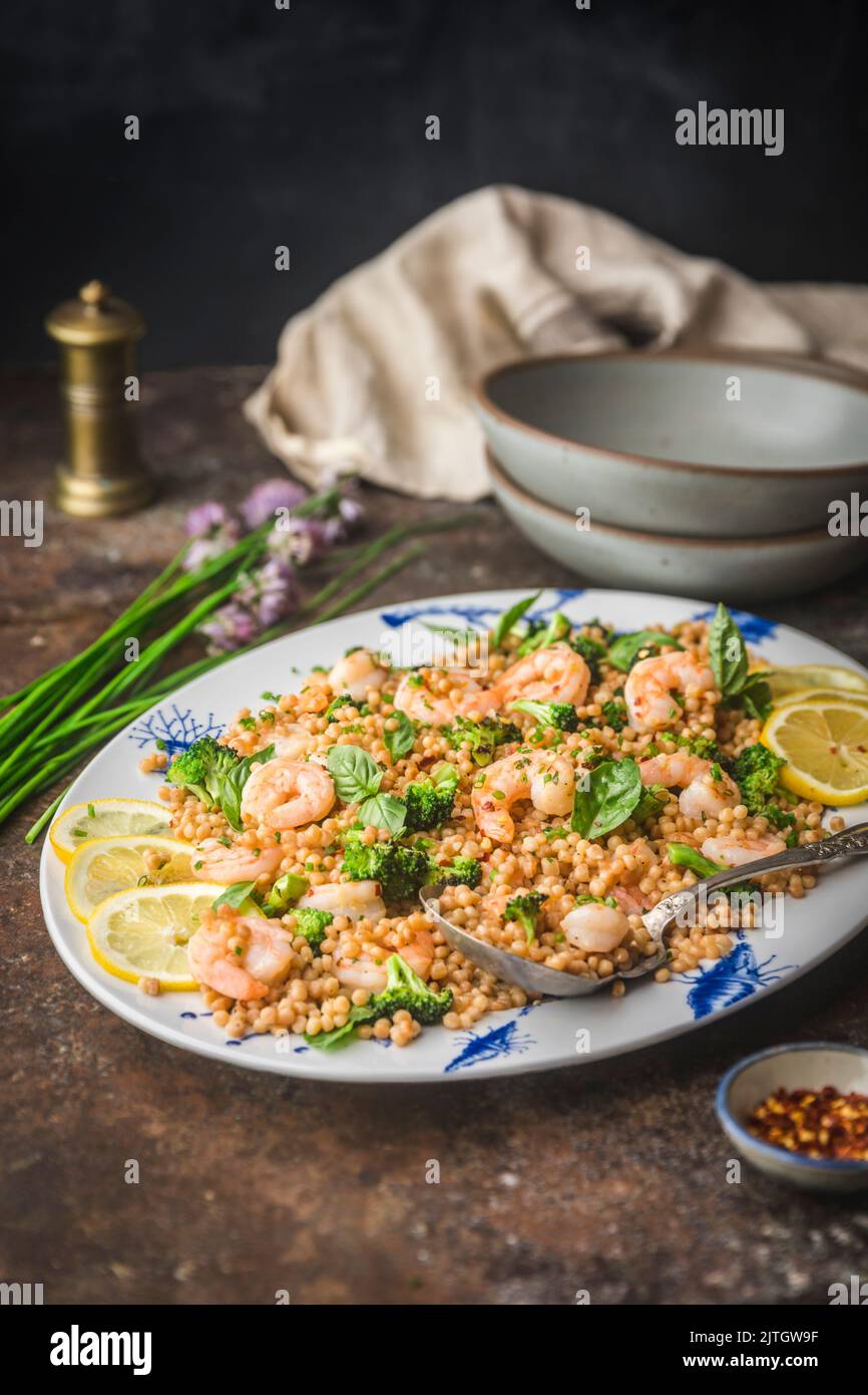 Shrimp with Pearl Couscous and Broccoli on Platter with herbs and serving bowls Stock Photo
