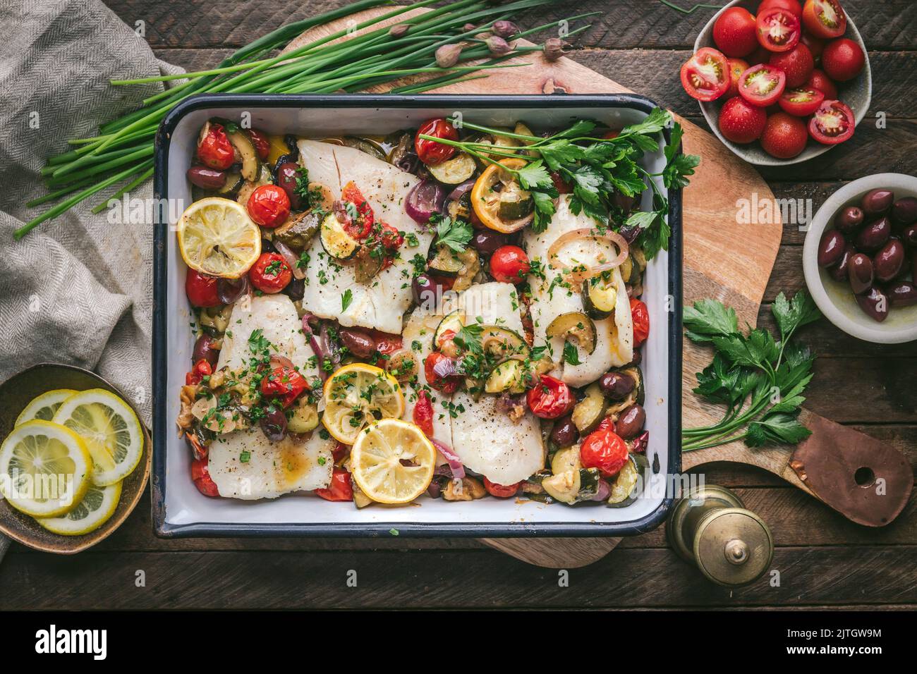 Roasted Fish Filets in enamel baking dish with tomatoes, courgette, olives and lemon Stock Photo