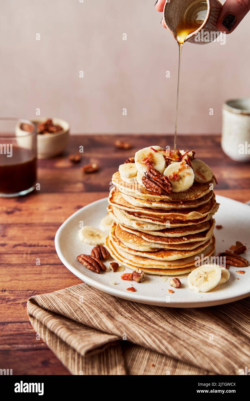 Banana Pecan Maple Syrup Drizzle Pour Pancakes on plate with coffee Stock Photo