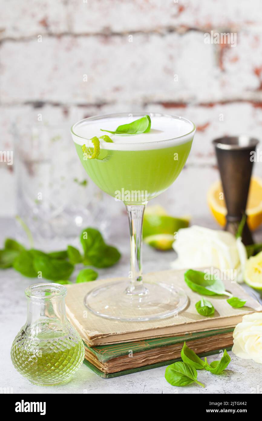 A green cocktail made with basil, lime and gin garnished with egg white