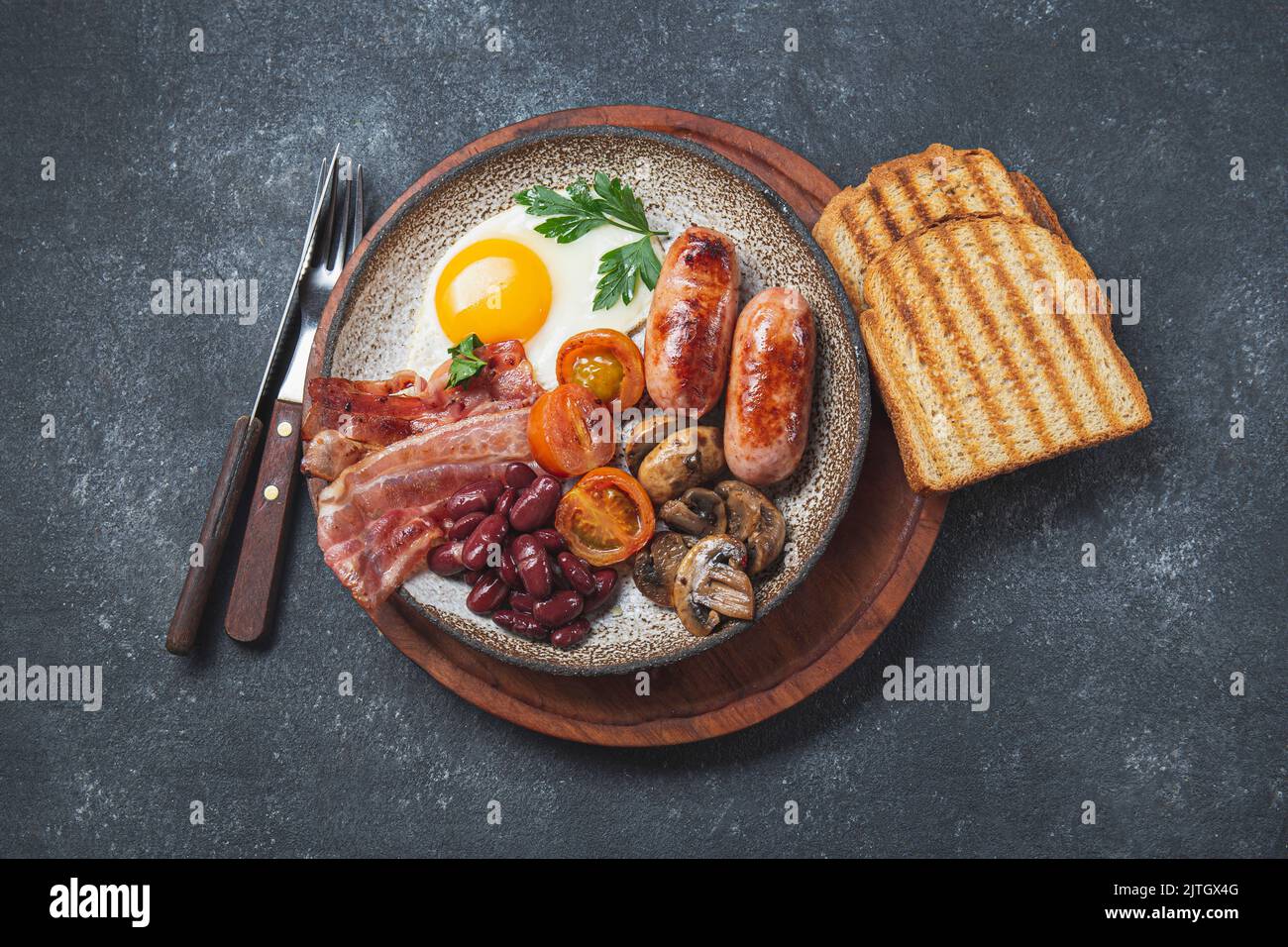 Traditional full English breakfast with fried eggs, sausages, beans, mushrooms, grilled tomatoes, bacon and toasts on gray plates Stock Photo
