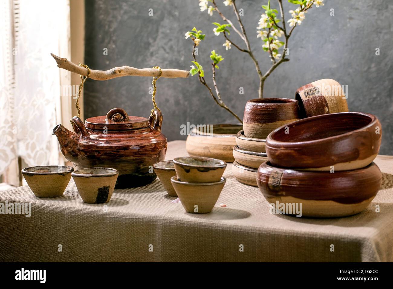 Japanese Asian style table setting with empty craft ceramic tableware, brown rough bowls and cups on linen tablecloth, decorated by ikebana spring flo Stock Photo