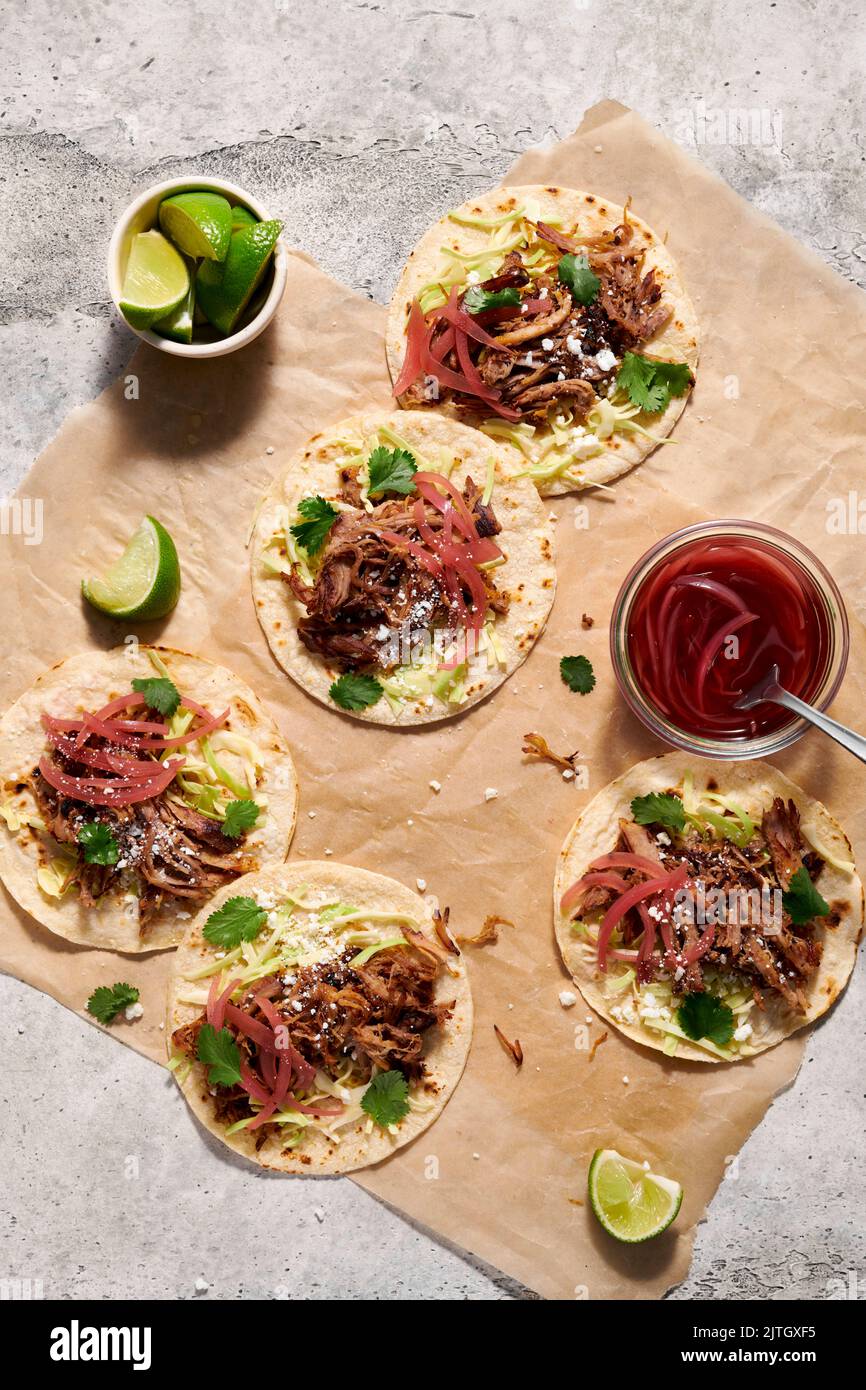 Five pork tacos with pickled red onions laid out on parchment paper