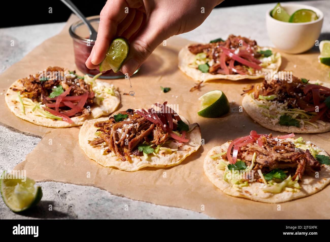 A hand squeezing a lime over pork tacos with pickled red onions Stock