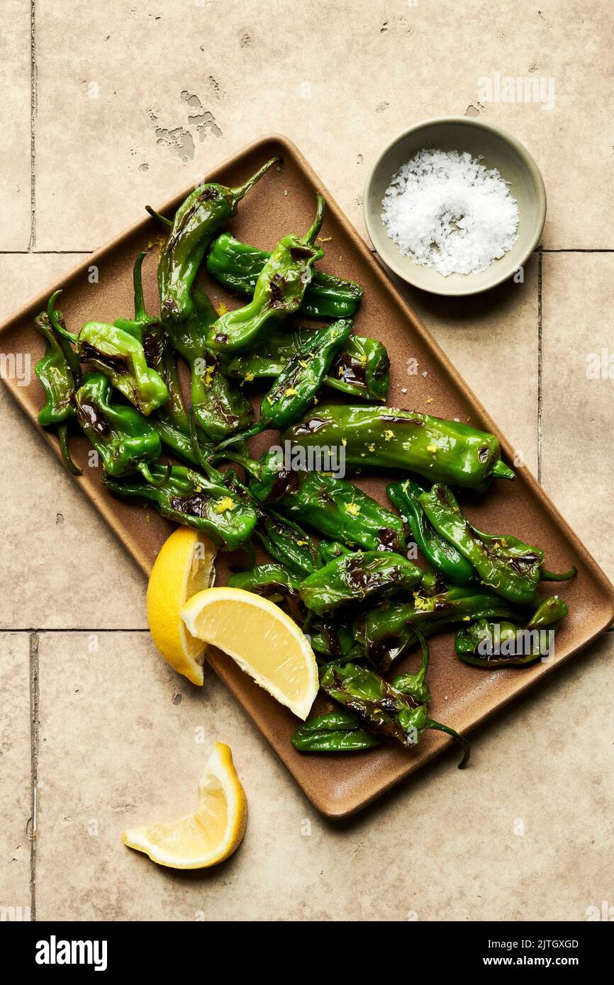 Blistered shishito peppers on a platter with lemon zest and sea salt. Stock Photo