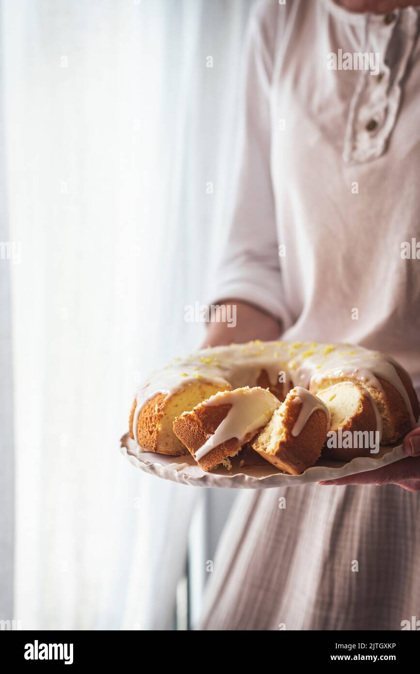 Lemon icing on a sponge bundt cake held by a woman in a dress Stock Photo