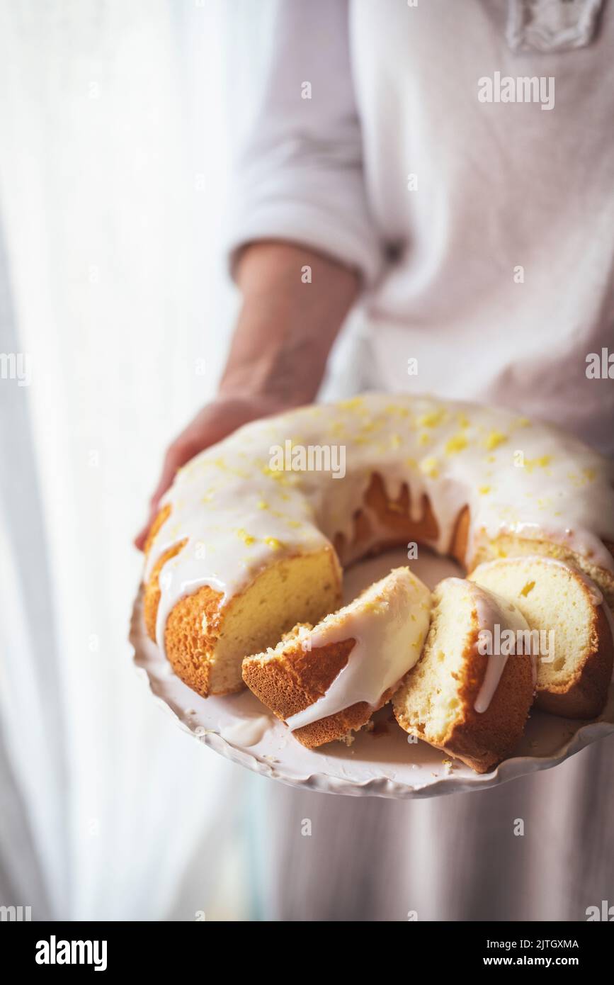 Lemon icing on a sponge bundt cake held by a woman in a dress Stock
