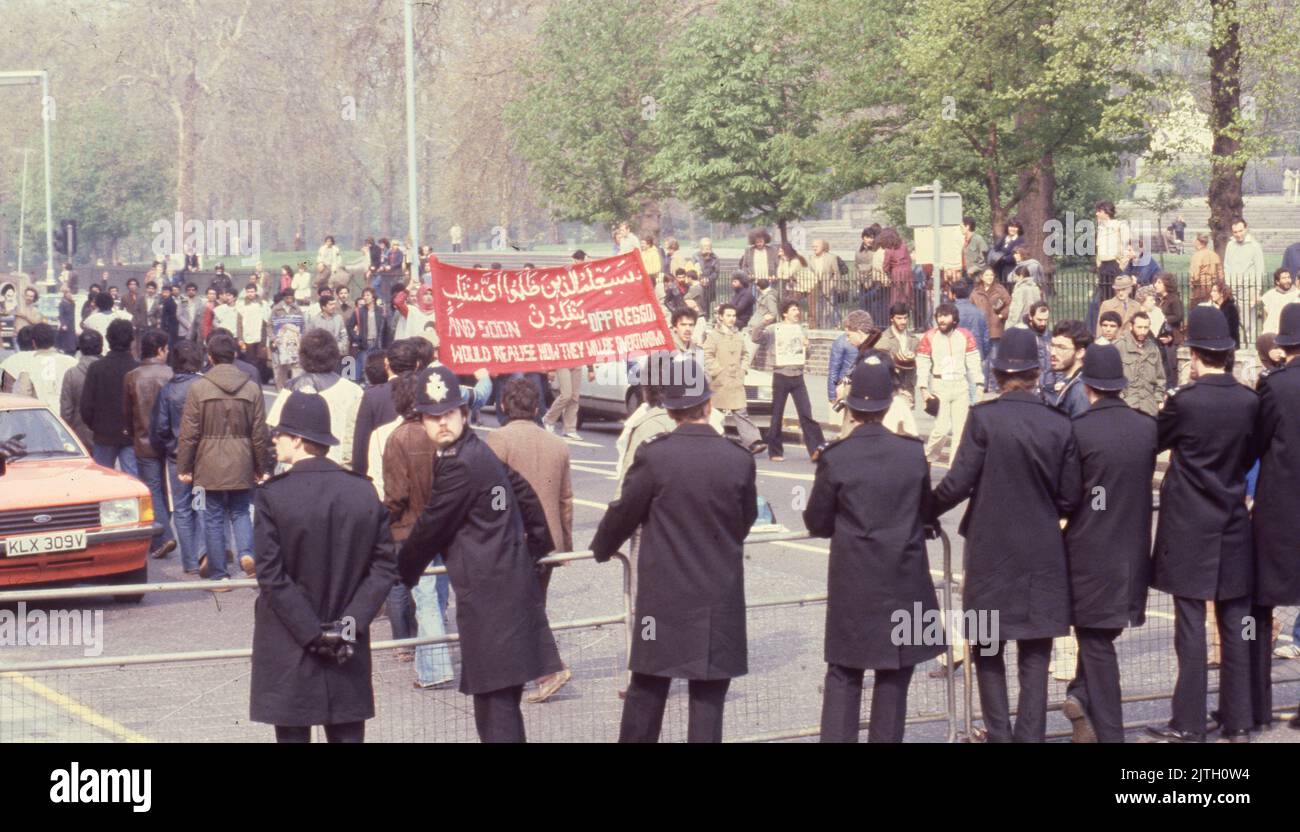 April 30, 1980, London, United Kingdom: Police on crowd control of the Iranian supporters carrying a banner the protest march in London during the six-day siege of the Iranian Embassy. From 30 April to 5 May 1980, a group of six armed Iranian dissidents, opposed to Ayatollah Khomeini, the religious leader who came to power in 1979, took over the Iranian embassy on Prince's Gate in South Kensington, London. The Iranian group took 21 hostages two of whom were killed. Near to the scene of the siege, supporters of Khomeini made their views known with a protest. The dramatic six-day siege ended whe Stock Photo