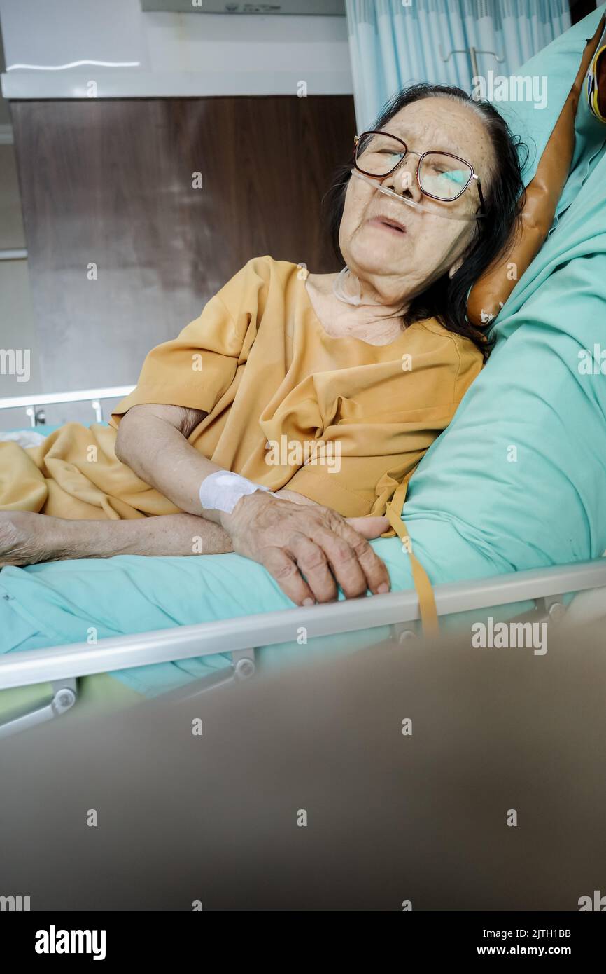 Sick Southeast Asian female senior patient with respiratory disorder having bedrest in hospital Stock Photo