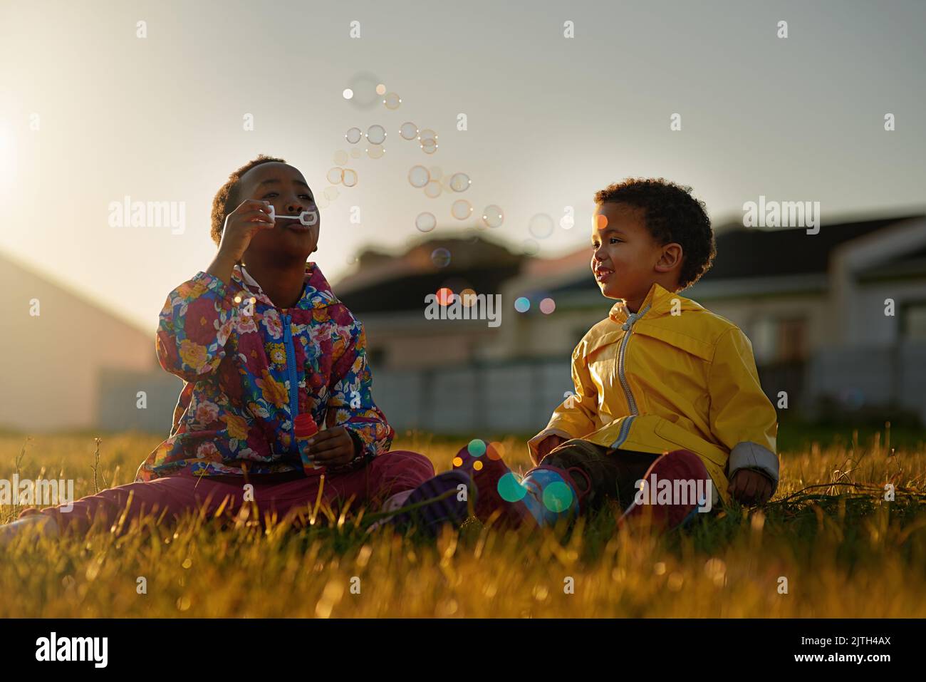 Enjoying a bit of bubble fun together. a brother and sister sitting on the ground outside blowing bubbles. Stock Photo