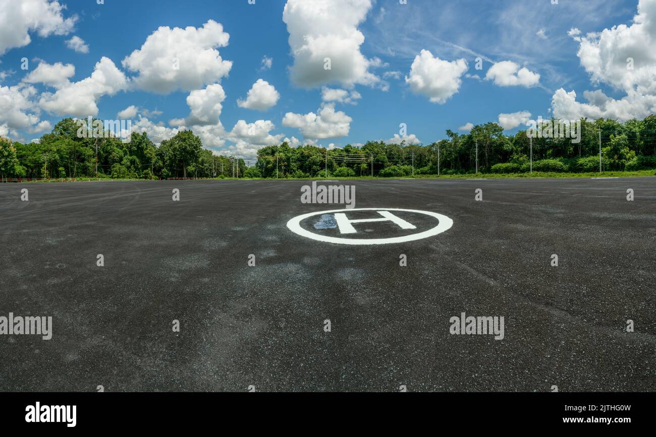 Asphalt helipad in the forest. Landscape of helipad. Helipad area against blue sky and white cumulus clouds in sunny day. Platform for helicopters Stock Photo