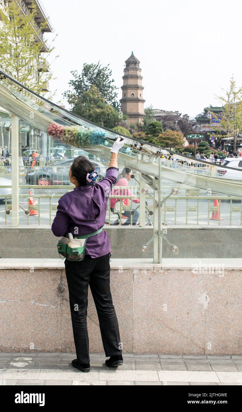 Chinese woman street cleaner dusting dust from glass railing leading to subway station Stock Photo