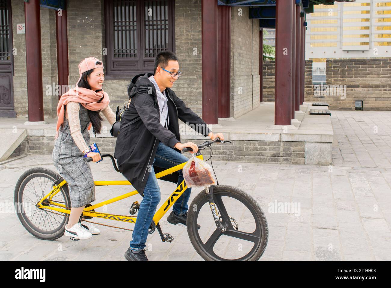 A  young Chinese couple having fun riding a tandem bicycle along Xi'an City Wall. Stock Photo