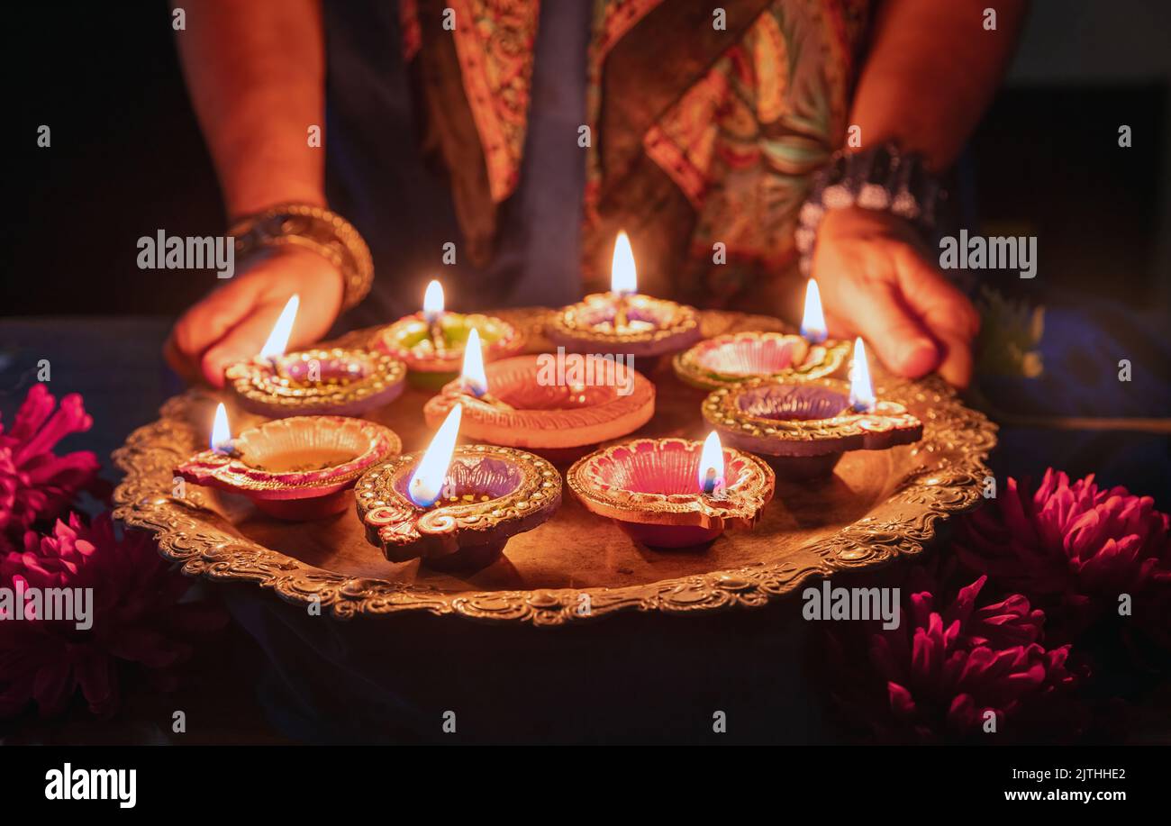 Diwali. Woman holding a tray with Diya oil lamps lit, Deepavali celebration. Hindu Festival of lights outdoors, India streets. Stock Photo