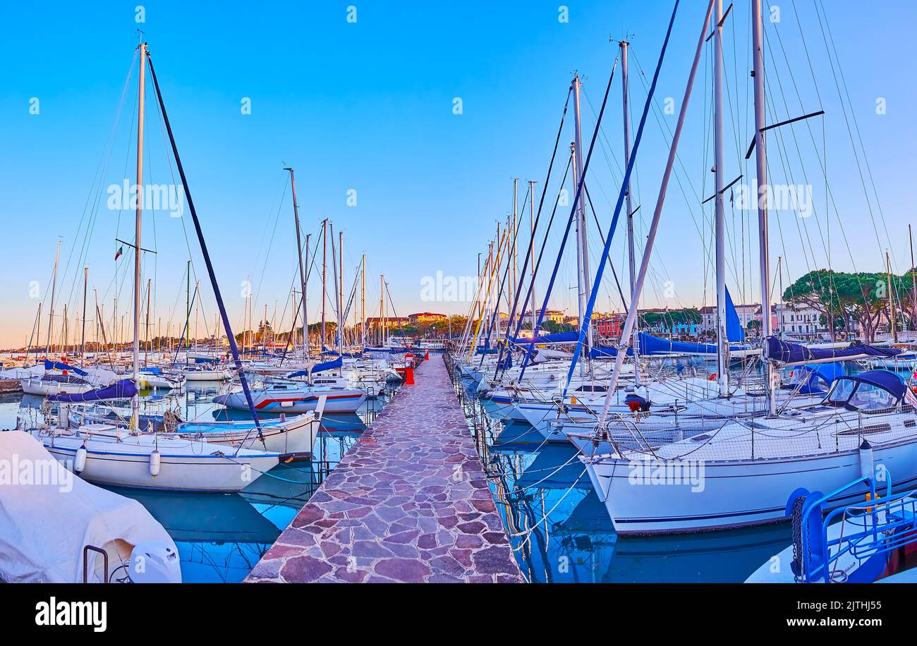 The shipyards with yachts and boats in front of the old stone lighthouse in port of Desenzano del Garda, Lake Garda, Italy Stock Photo