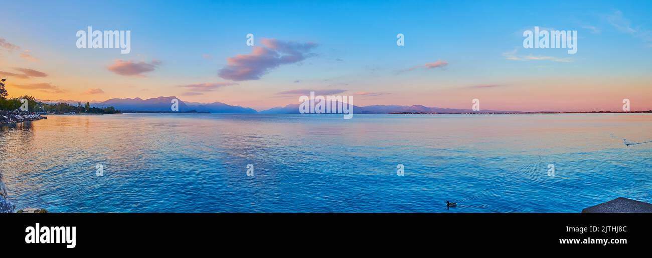 Panorama of the mirror-like Lake Garda on purple sunset with silhouettes of Garda Prealps mountains in the background, Desenzano del Garda, Italy Stock Photo