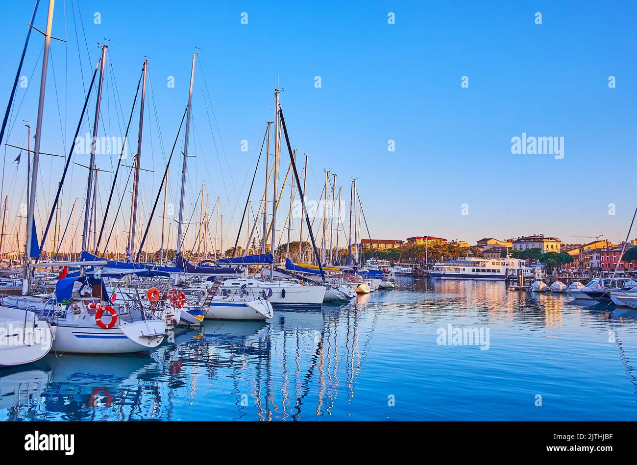 Lake Garda azure surface with moored sail yachts and houses in background at sunset, Desenzano del Garda, Italy Stock Photo