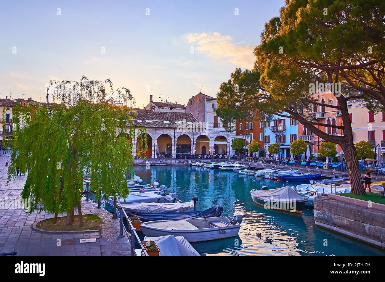 The lines of moored fishing boats in a small Porto Vecchio (Old Port), surrounded with old town housing in a bright sunset light, Desenzano del Garda, Stock Photo